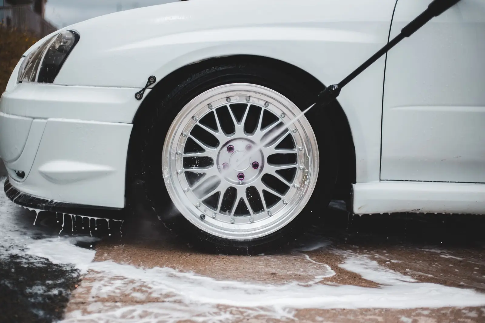 A jet wash lance rinsing foam off a car wheel